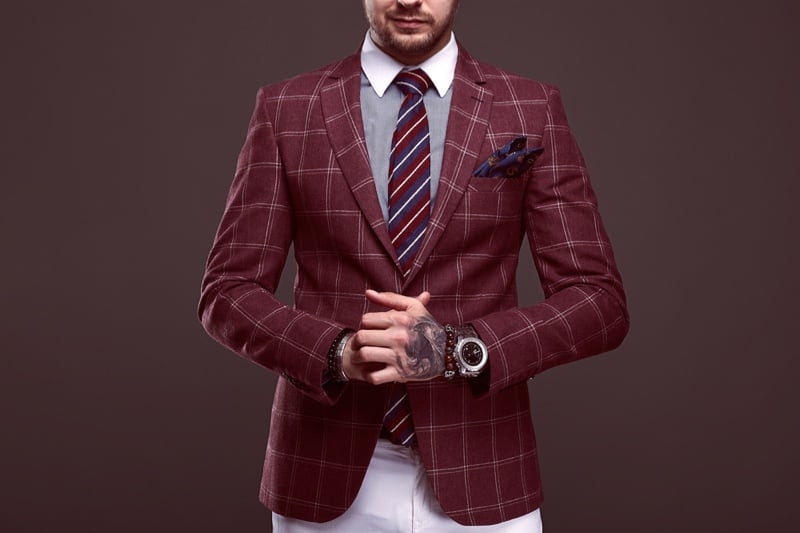 Man with hand tattoo wearing burgundy blazer with white pants