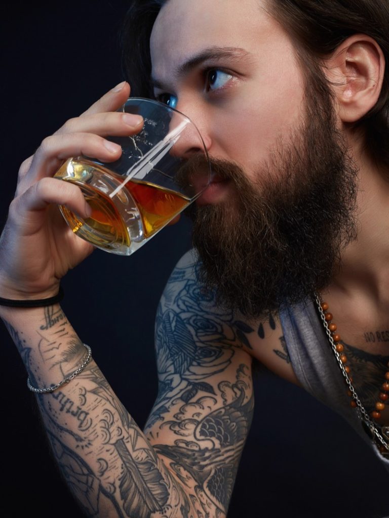 Man with tattoos drinking whiskey