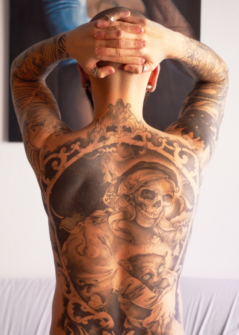 Full back piece in black and gray featuring a pirate skull with hat, ornamental baroque frame, and cat figure, spanning from neck to lower back.