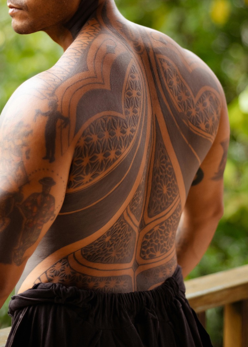 Large-scale geometric blackwork tattoo with mandala and ornamental patterns covering a man's full back in dense black ink with skin-tone negative space.