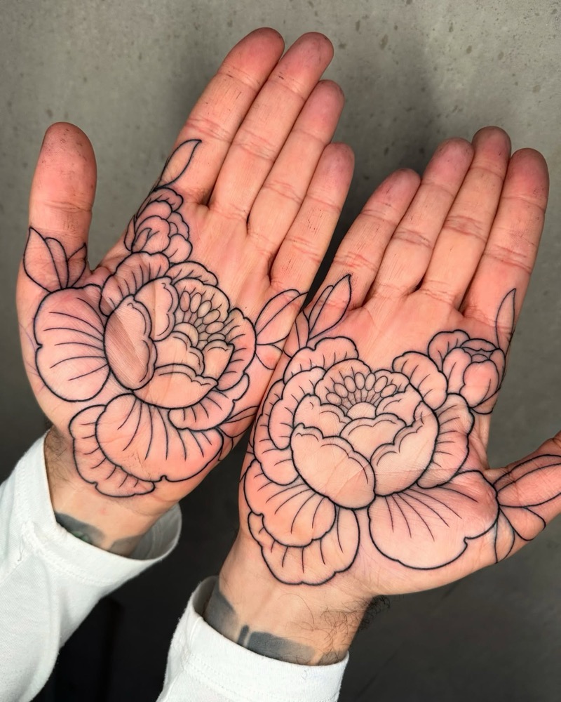 Two open palms facing the camera, each tattooed with a large outlined peony flower in black linework that covers most of the palm.