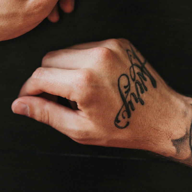 A cursive script lettering tattoo in bold black ink across the back of a man's hand.